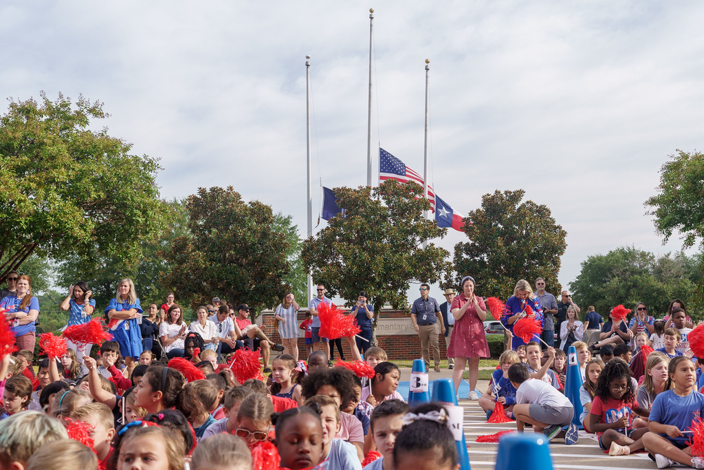 crowd under flags at half staff